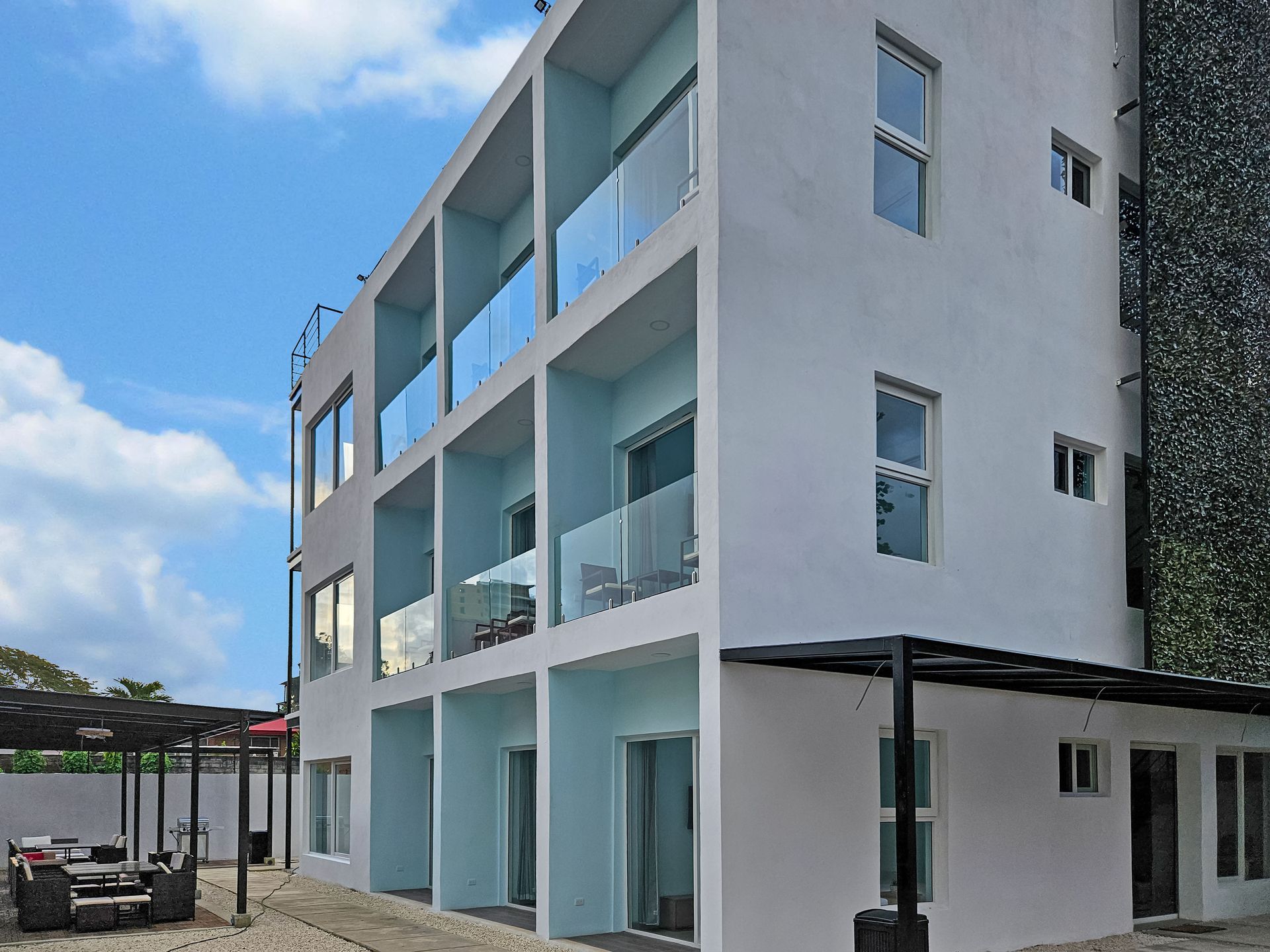 Multi-story white building with balconies and outdoor seating under a canopy.