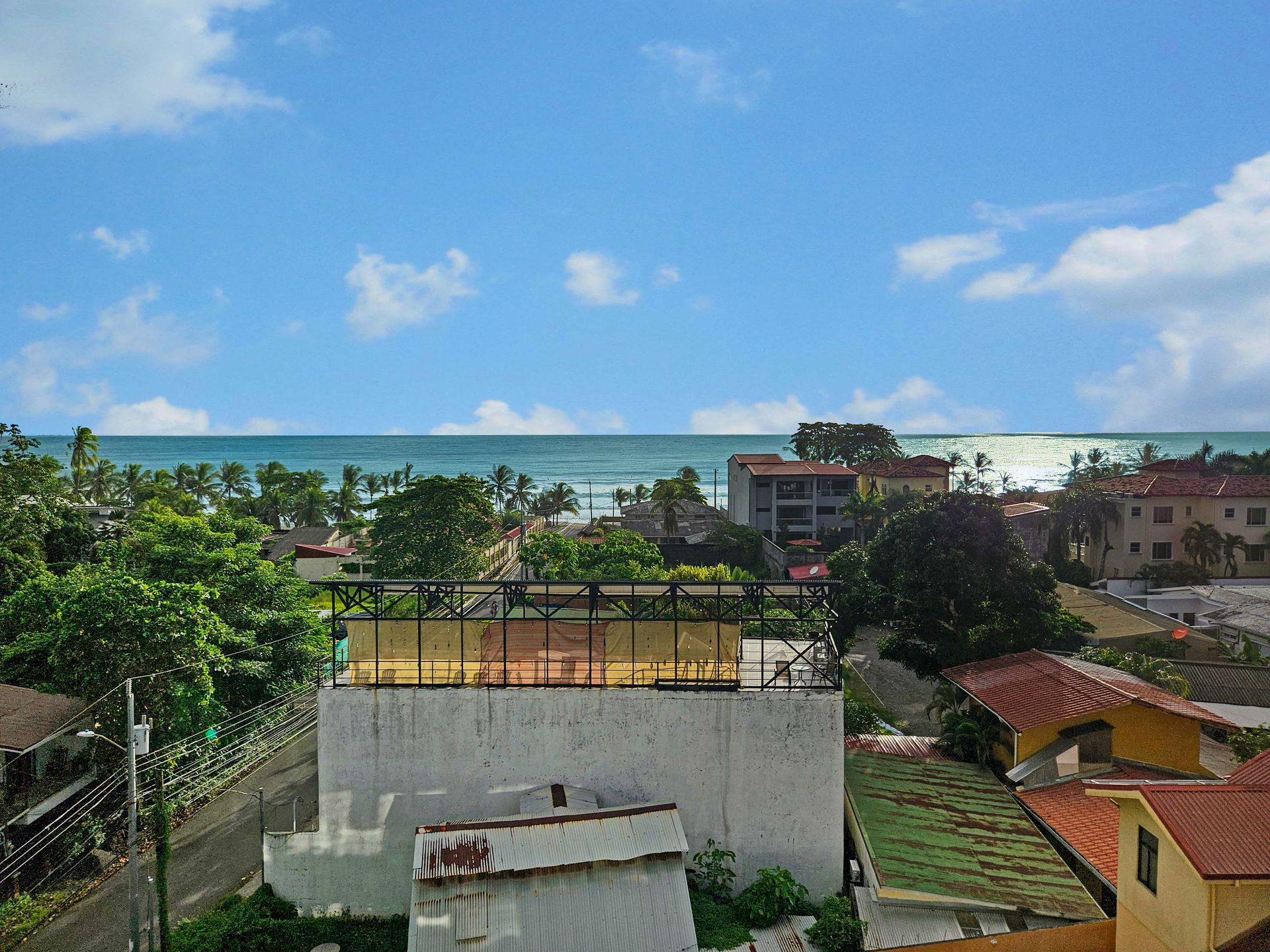 Rooftop view of the ocean, trees, and buildings under a blue sky with clouds.