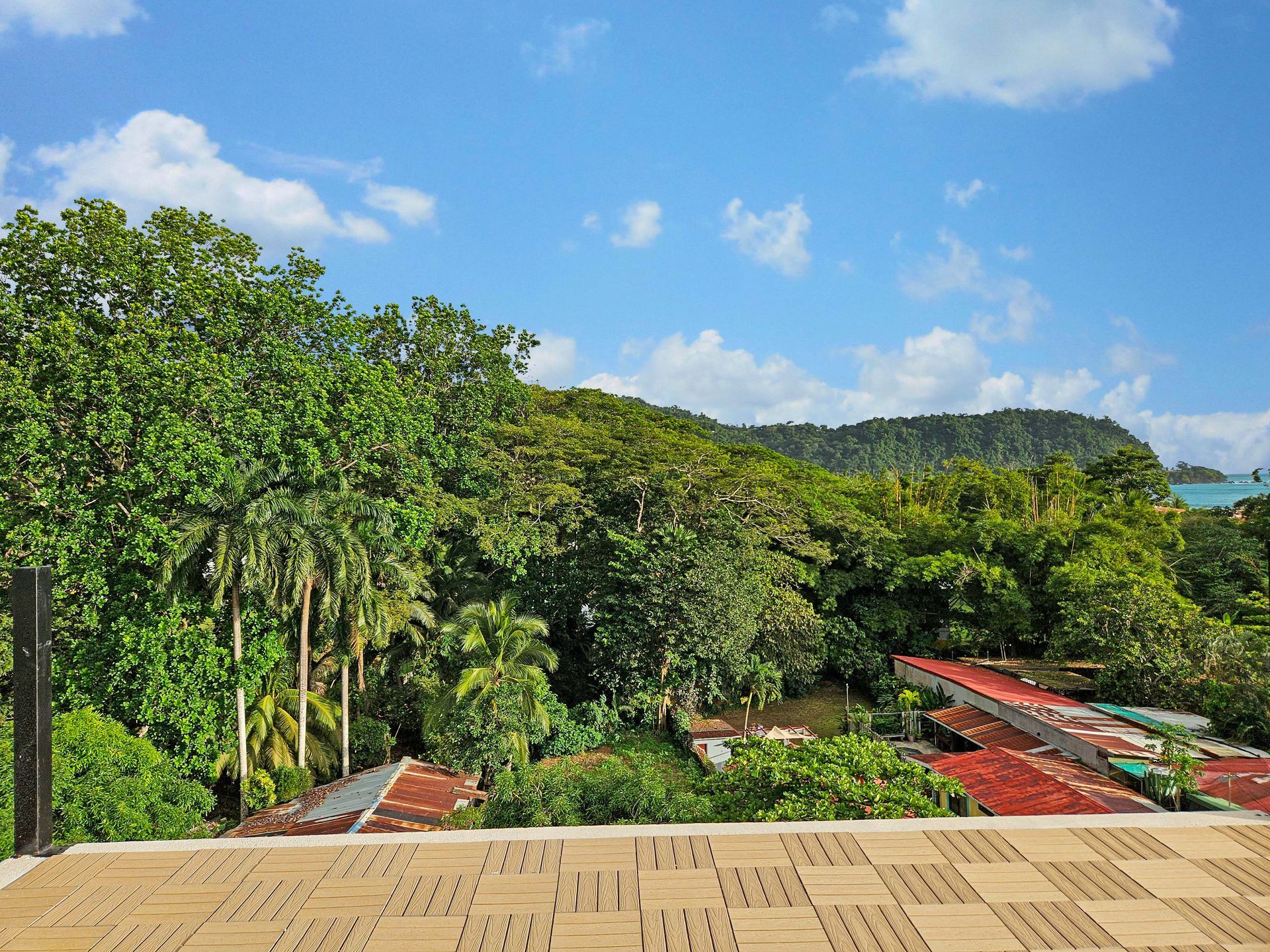 View of lush green trees, red rooftops, and a blue sky with clouds.