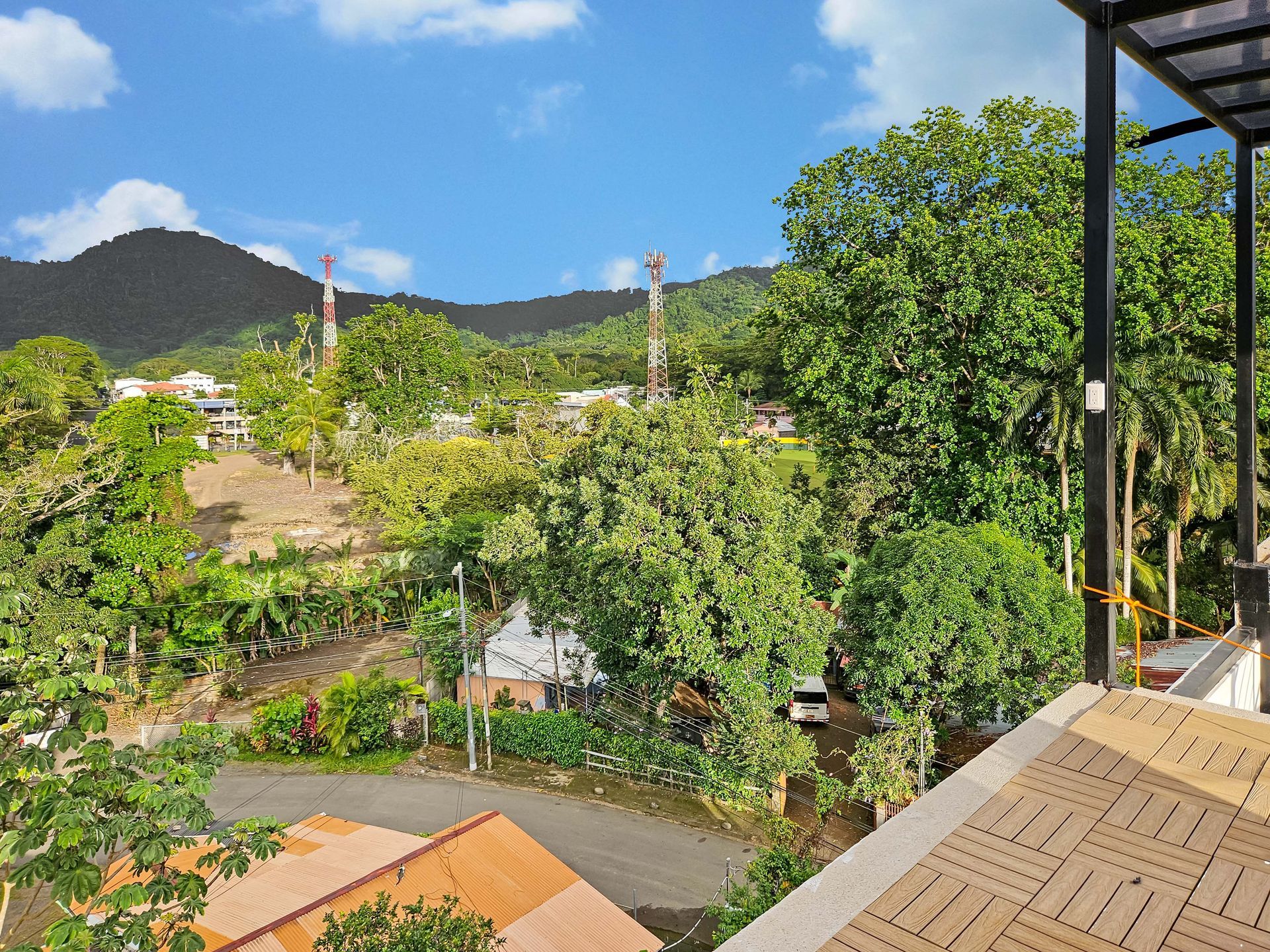 View of lush green trees, village and mountains under a blue sky, with some utility towers.