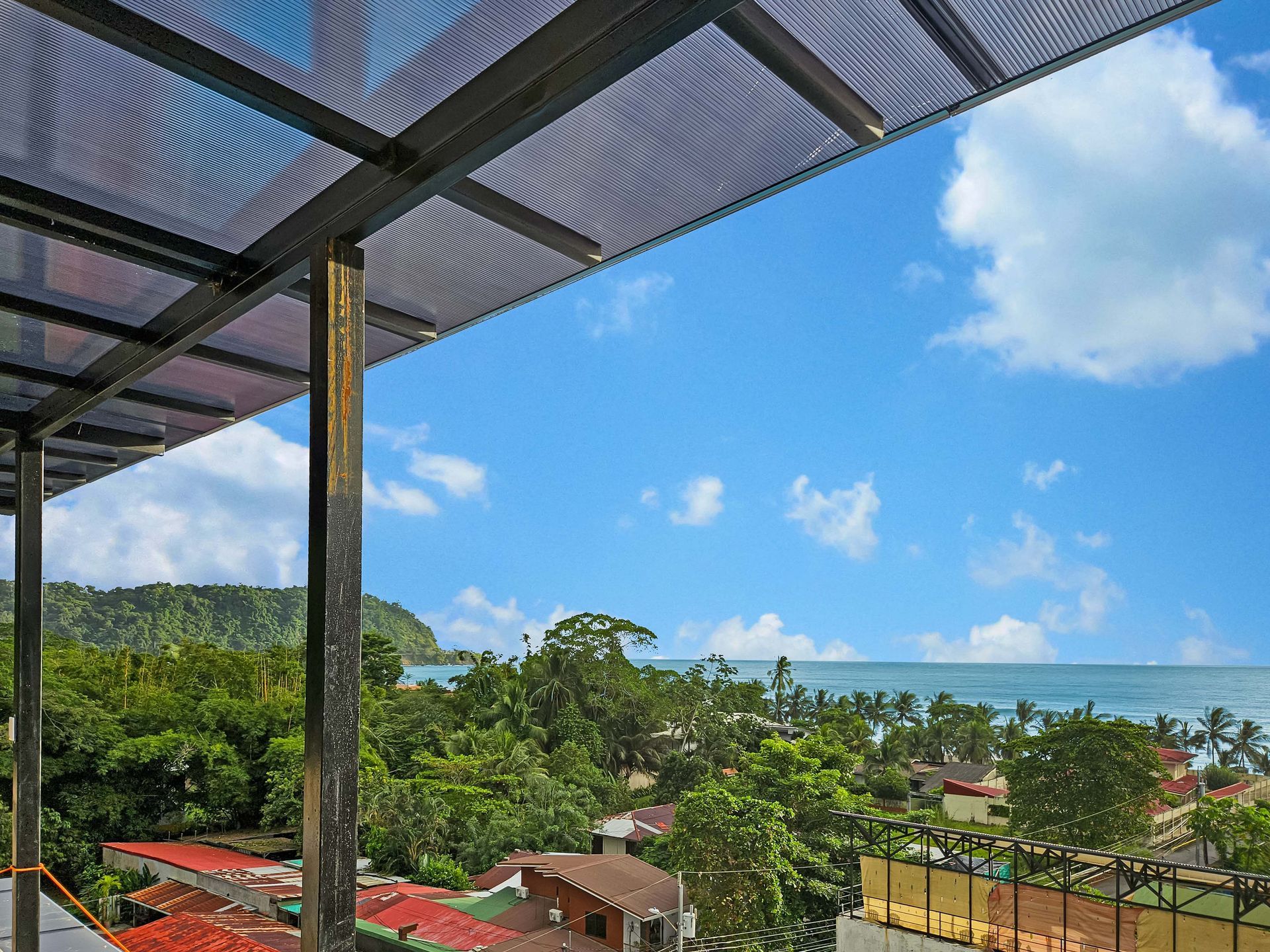 View from a covered balcony overlooking a green landscape, ocean, and blue sky.