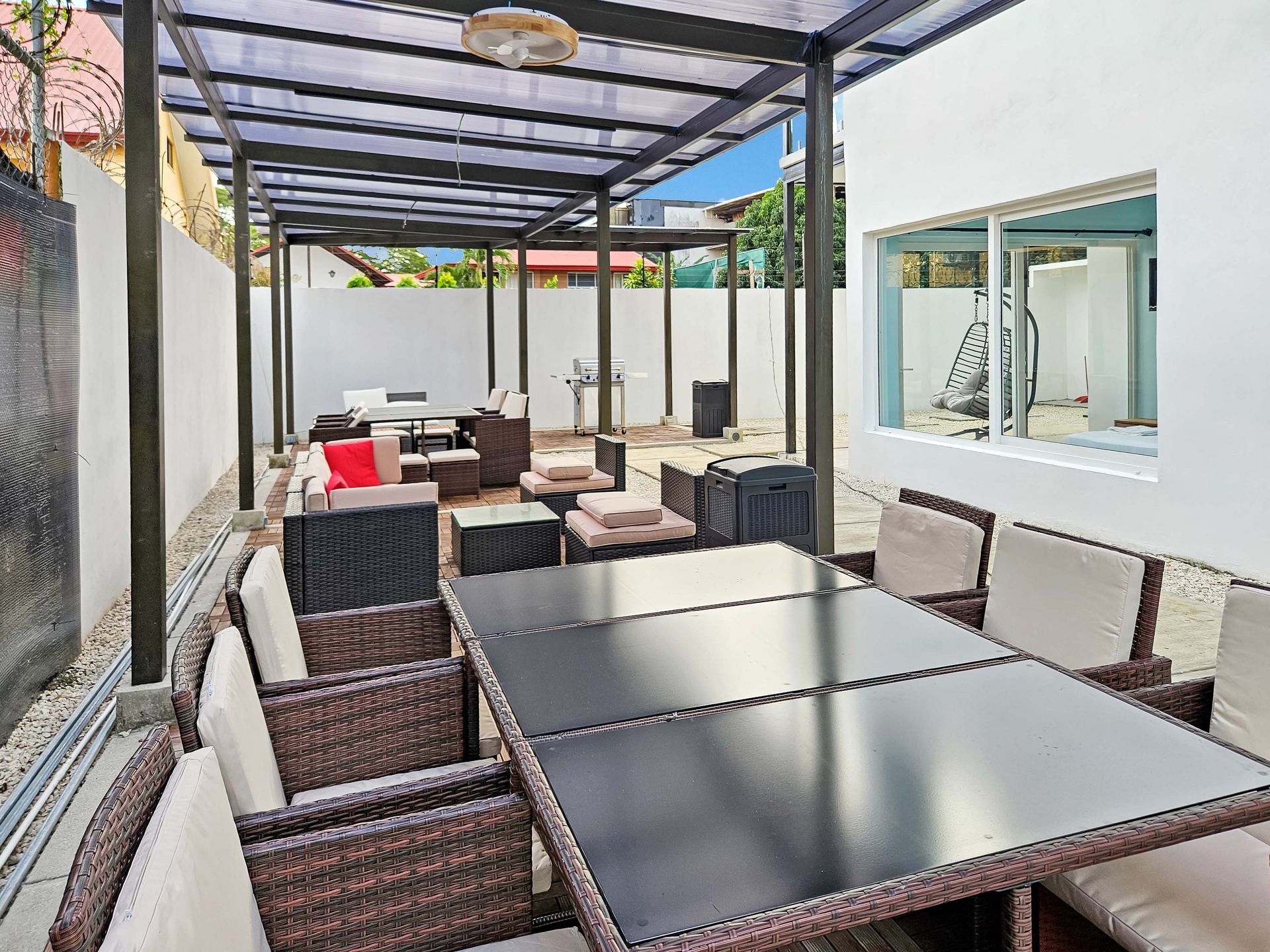 Outdoor patio with seating under a black pergola. White walls, black tables, and wicker chairs.
