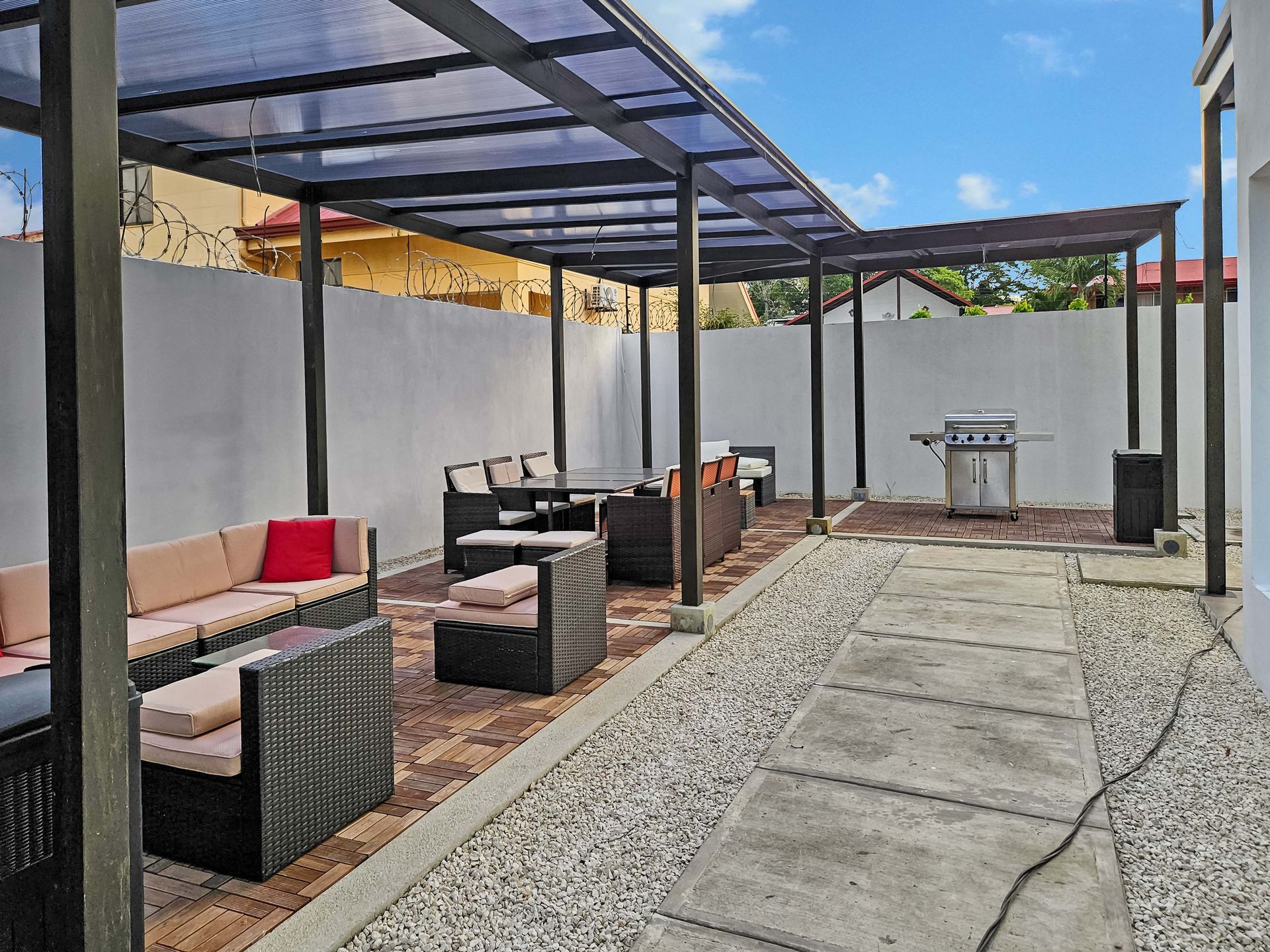Patio with seating, grill, and pergola covered with translucent panels. Grey, beige and black tones.