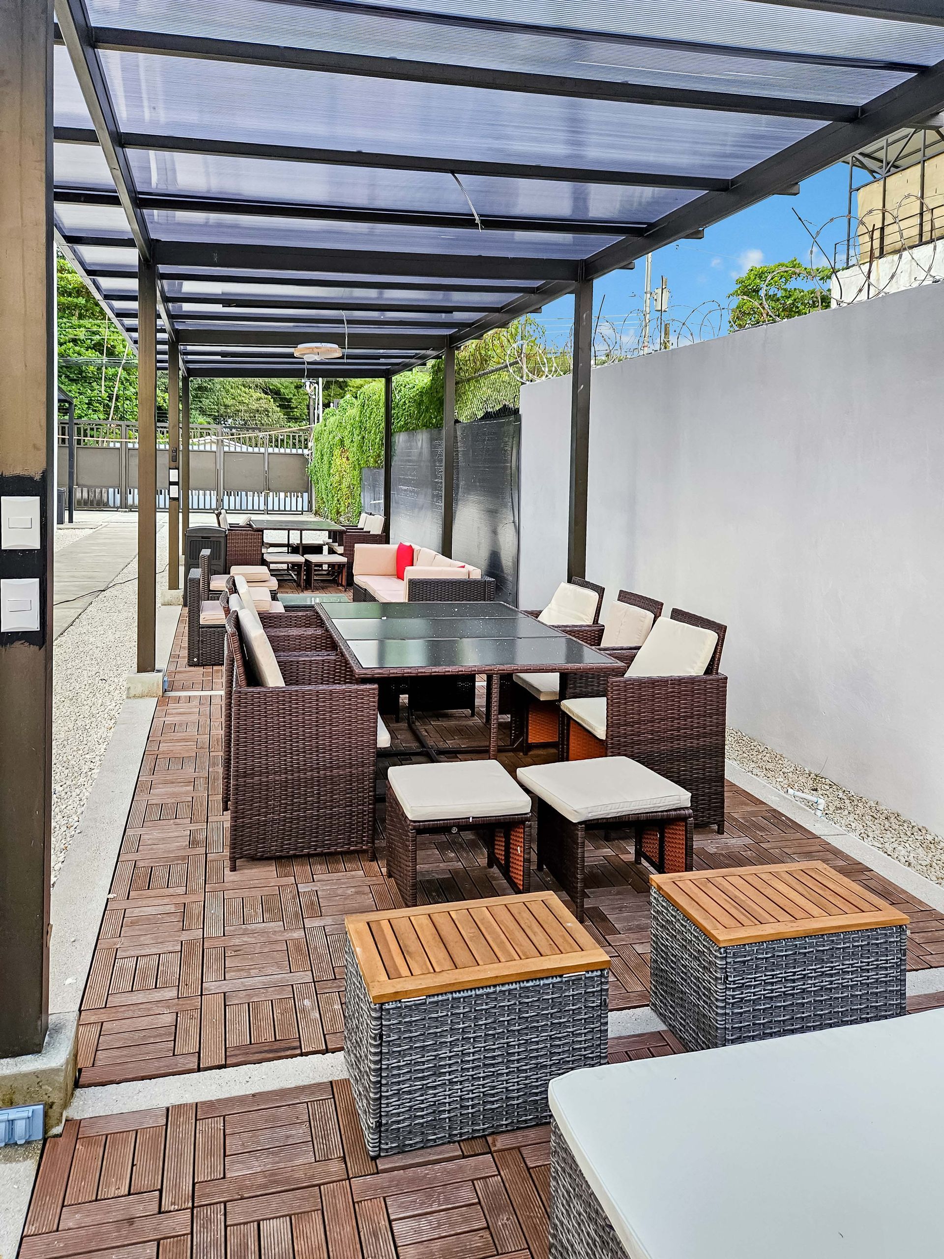 Outdoor dining area with woven furniture under a pergola with a translucent roof.