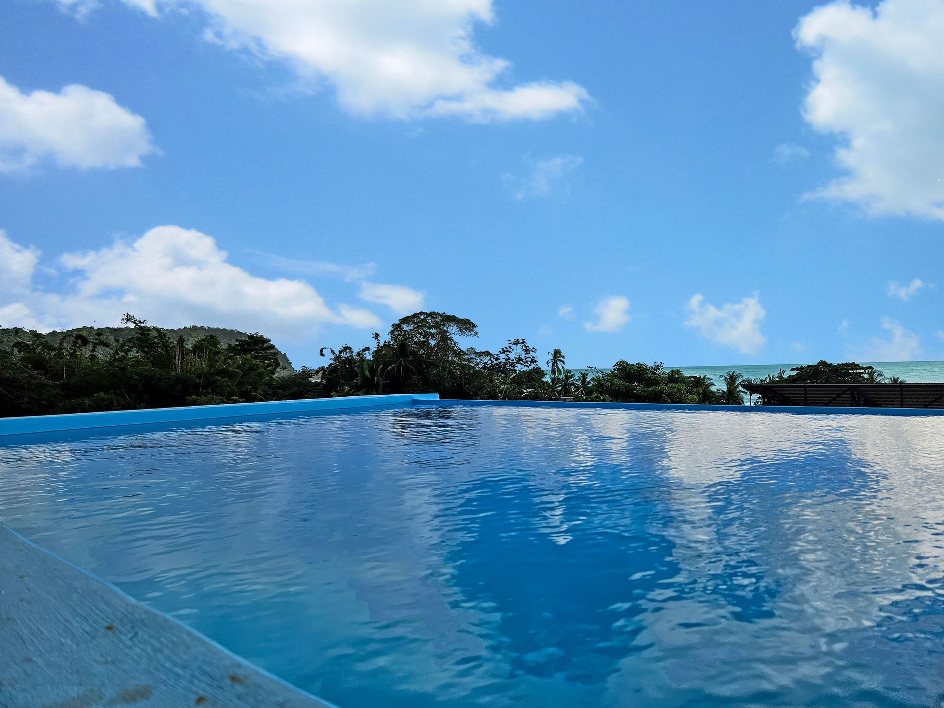 Swimming pool reflecting the bright blue sky and clouds; ocean in the background.
