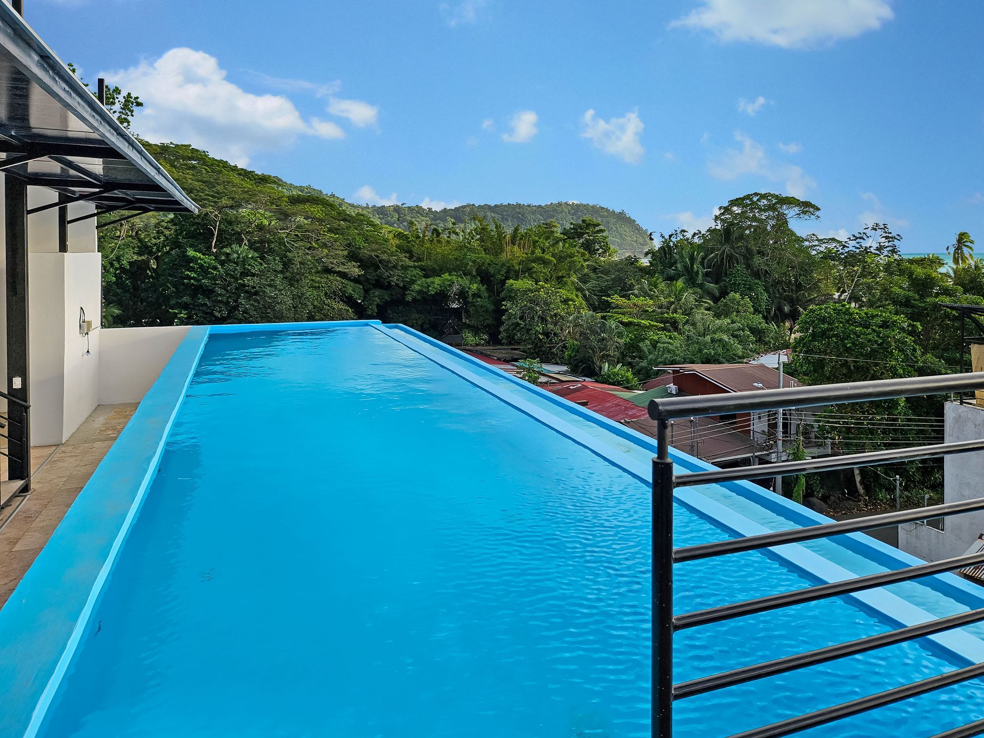 Rooftop infinity pool with turquoise water overlooking lush green trees and a blue sky.