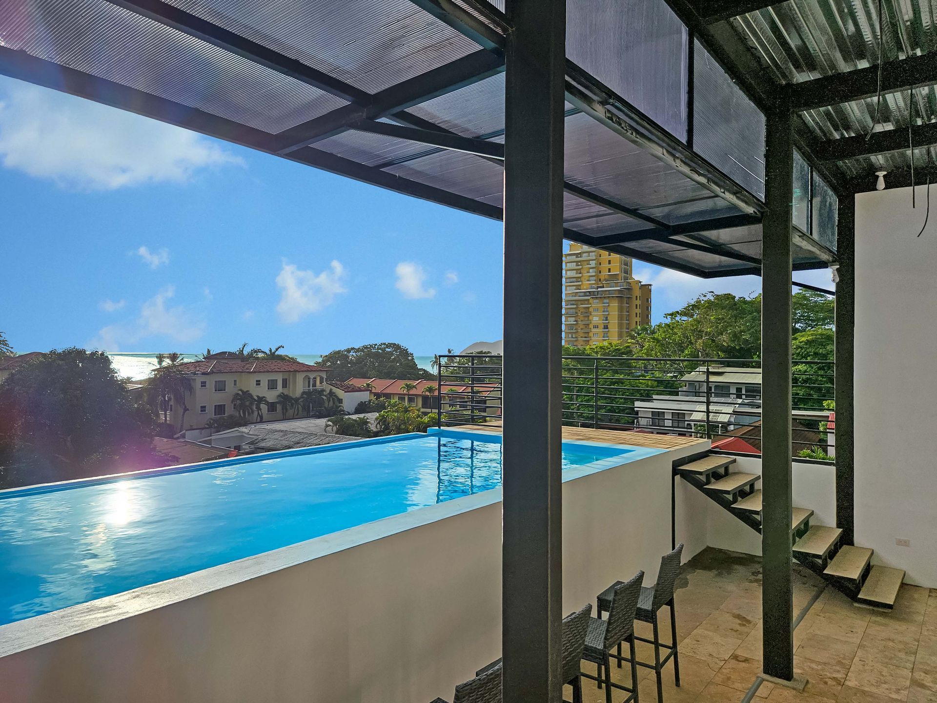 Outdoor infinity pool with a view, under a metal roof. Blue sky and sunny.