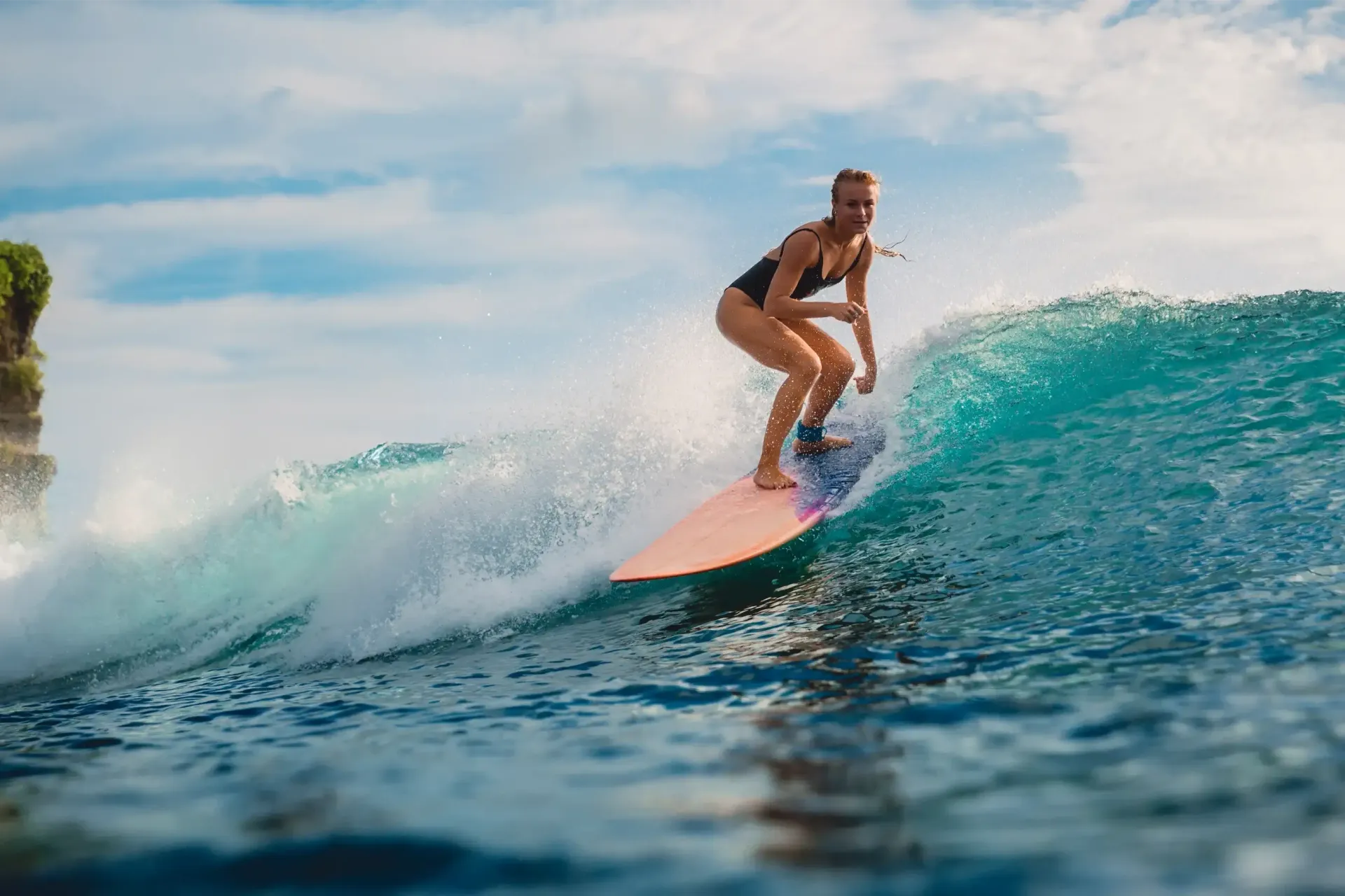Woman surfing on a wave, balancing on a pink surfboard in blue ocean.