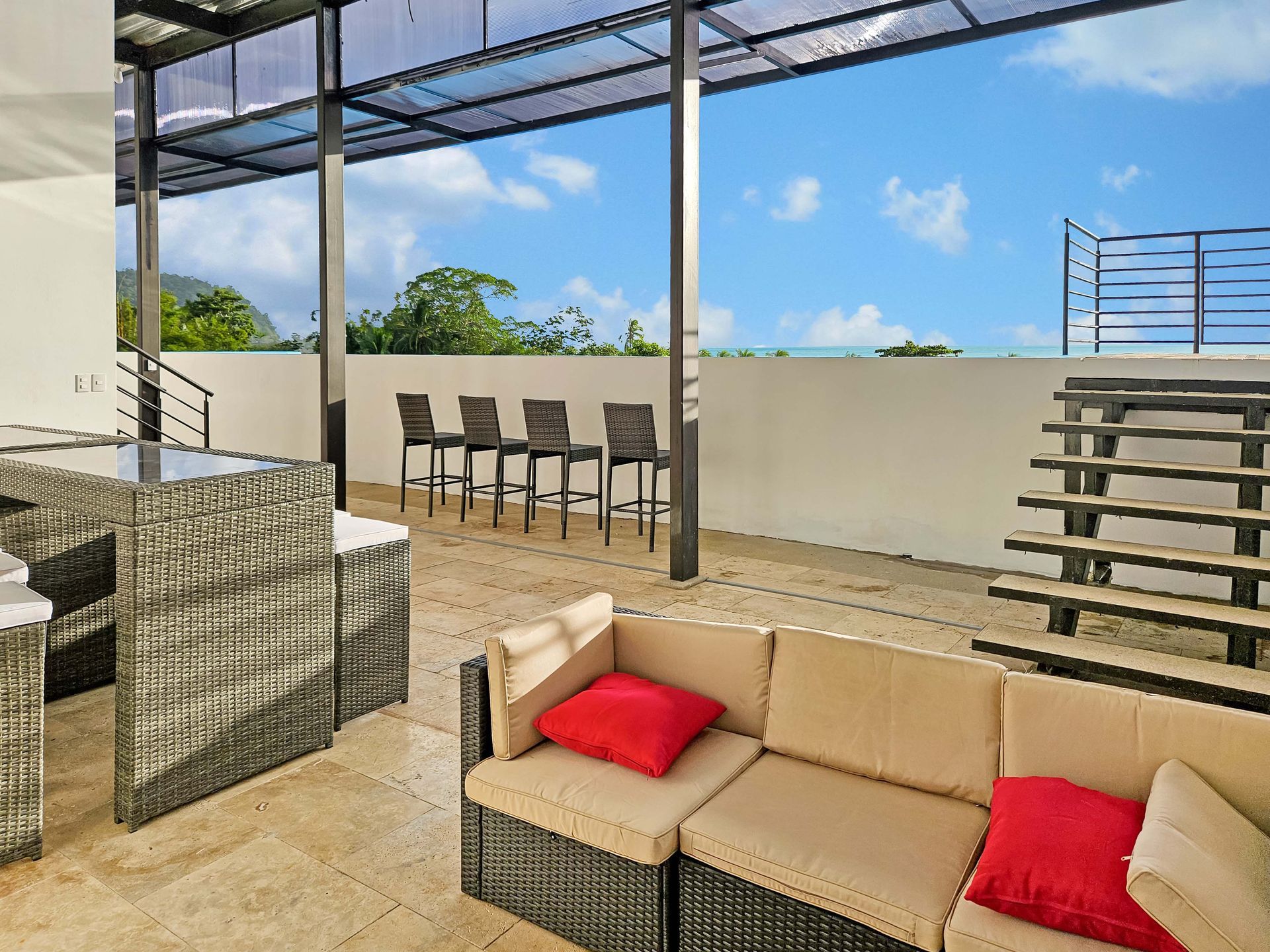 Outdoor patio with seating, table, and view of trees and sky.
