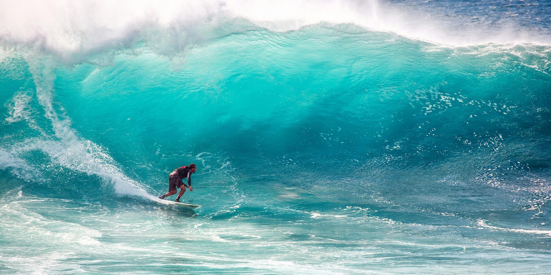 Surfer riding a large, turquoise wave.