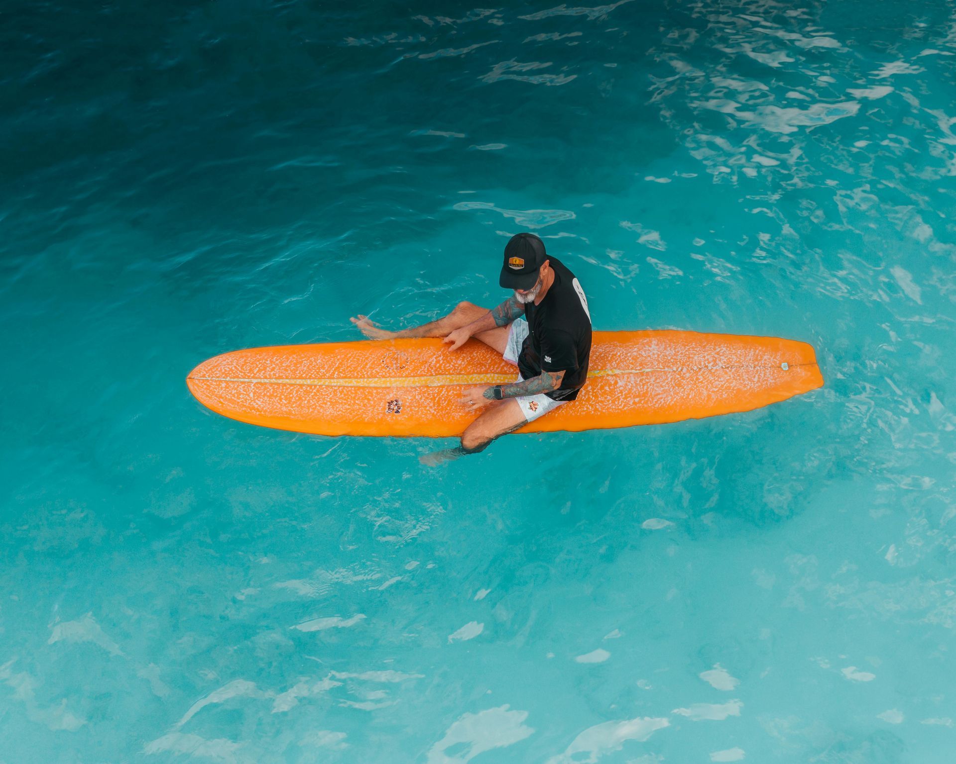 Person sits on orange surfboard in blue water.