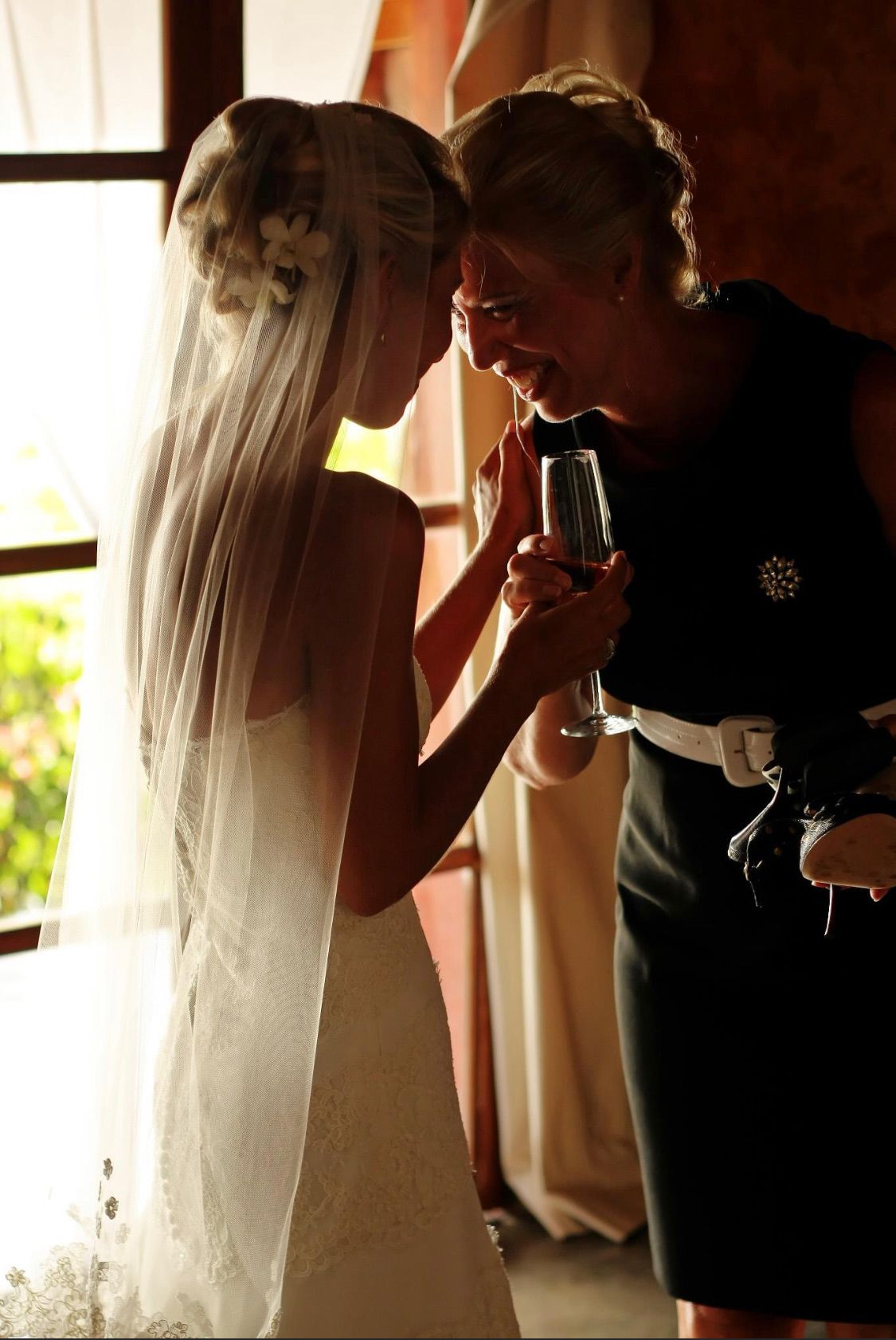 a woman in a black dress holds a glass of wine next to a bride in a white dress