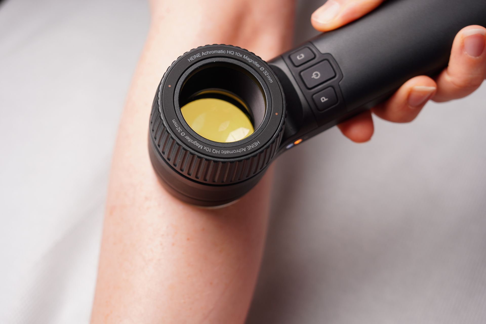 En handhållen hudanalysapparat på en persons arm, hållen i handen. Apparaten är svart med ett gult ljus.