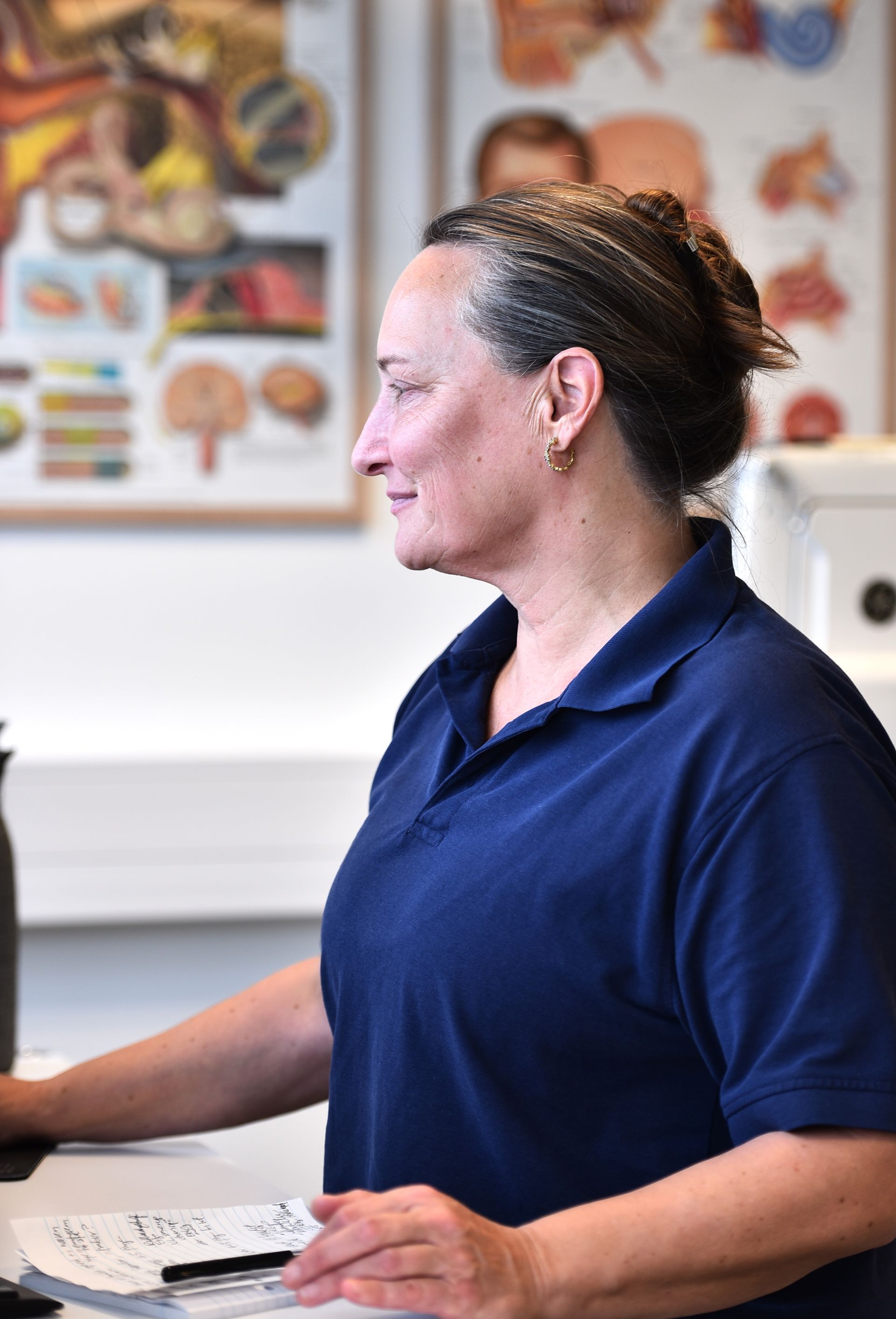 Kvinna med långt brunt hår, klädd i en mörkblå pikétröja, tittar in i kameran.