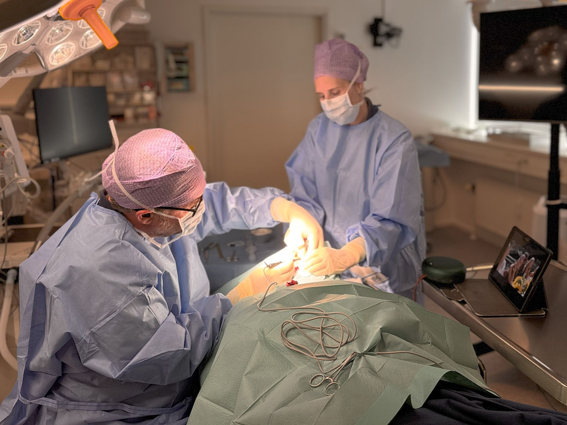 Två kirurger opererar en patient i en steril operationssal.