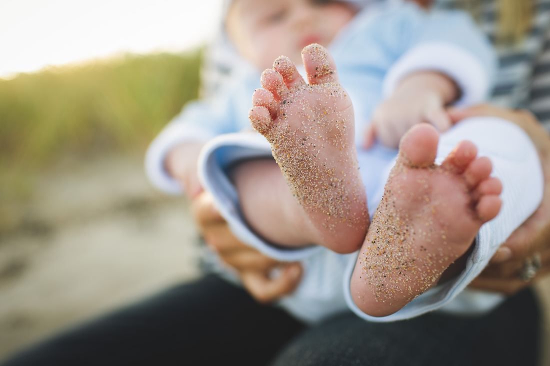 A person is holding a baby 's feet in the sand.