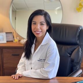 A woman in a lab coat is sitting at a desk in front of a mirror.