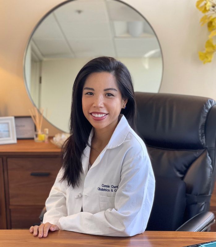 A woman in a white lab coat is sitting at a desk in front of a mirror.