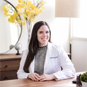 A woman in a white lab coat is sitting at a desk.