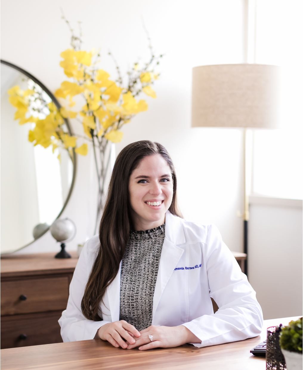 A woman in a white lab coat is sitting at a desk.