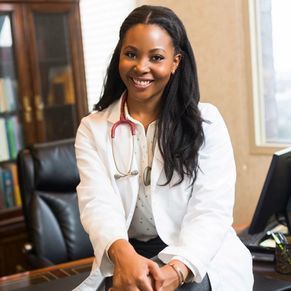 A female doctor is sitting at a desk with a stethoscope around her neck.