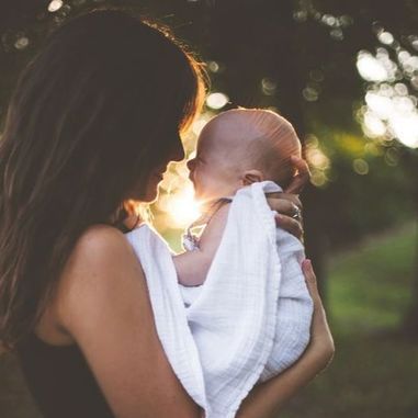 A woman is holding a baby wrapped in a white blanket.