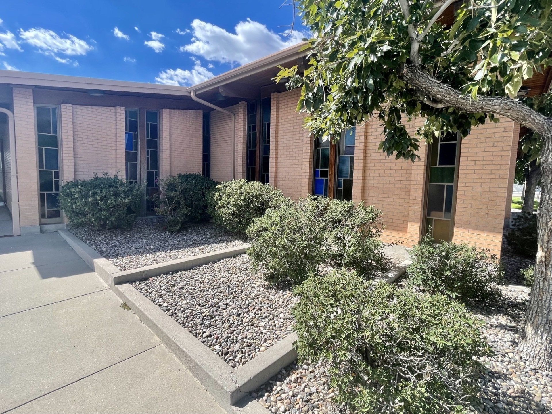 Beige stucco building with bell tower, arched windows, red tile roof, and blue sky.