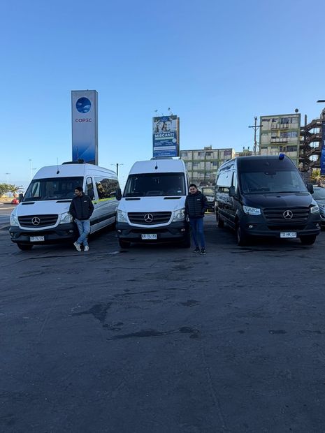 Trabajadores con chalecos reflectantes inspeccionan una fila de furgonetas blancas