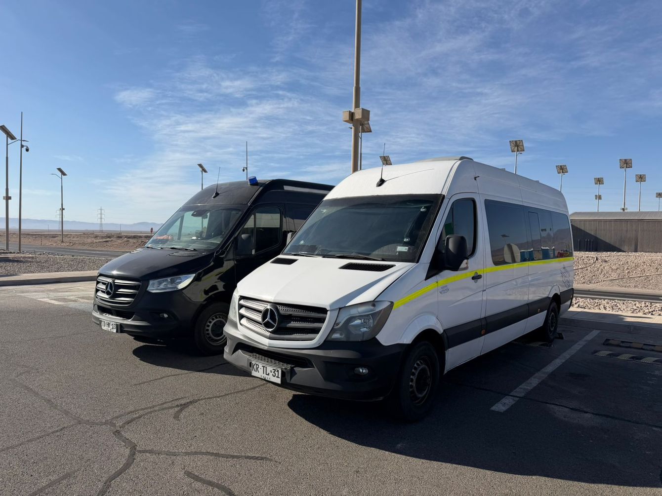 Una persona con uniforme azul se encuentra de pie frente a una furgoneta Mercedes-Benz blanca en una zona minera industrial.