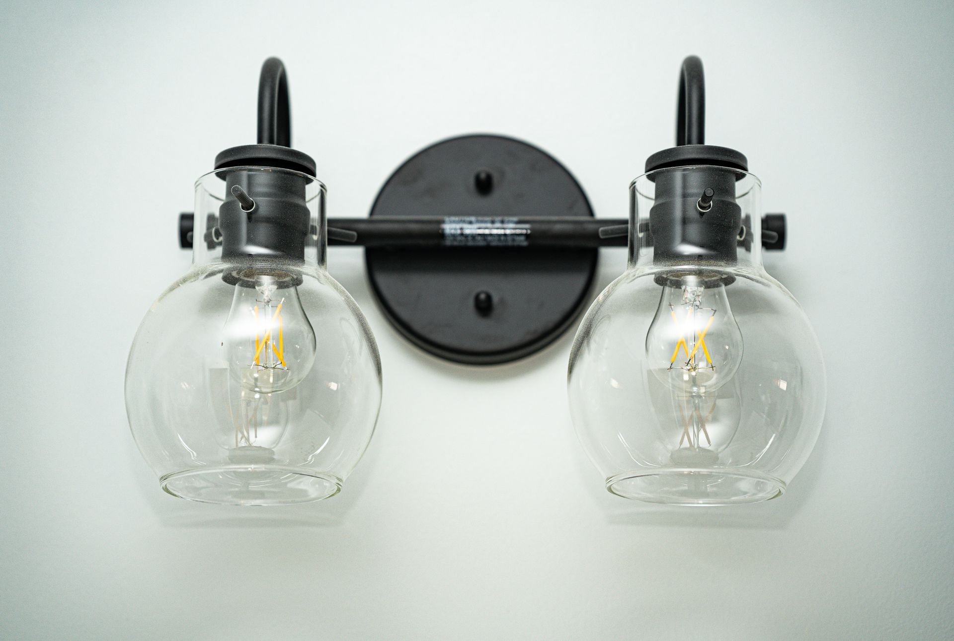 Black, two-bulb bathroom light fixture with clear glass globes, mounted on a white wall.