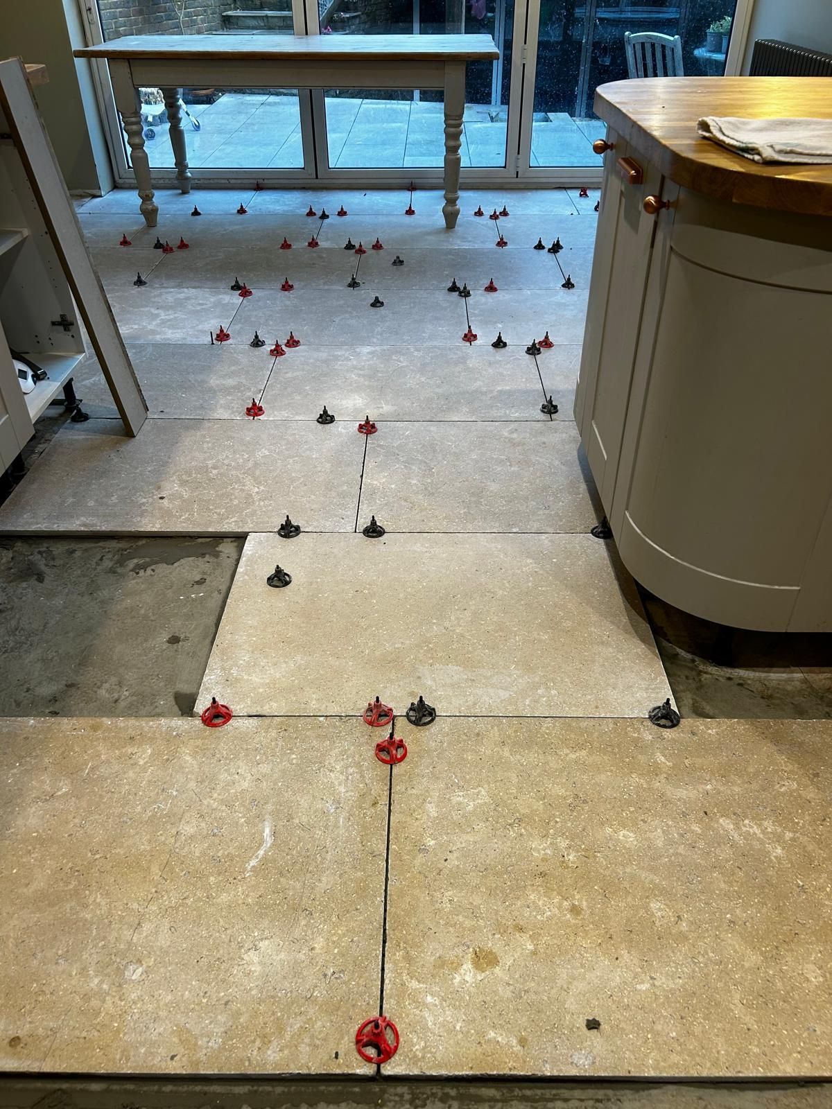 A kitchen floor with tiles being installed and a table in the background.