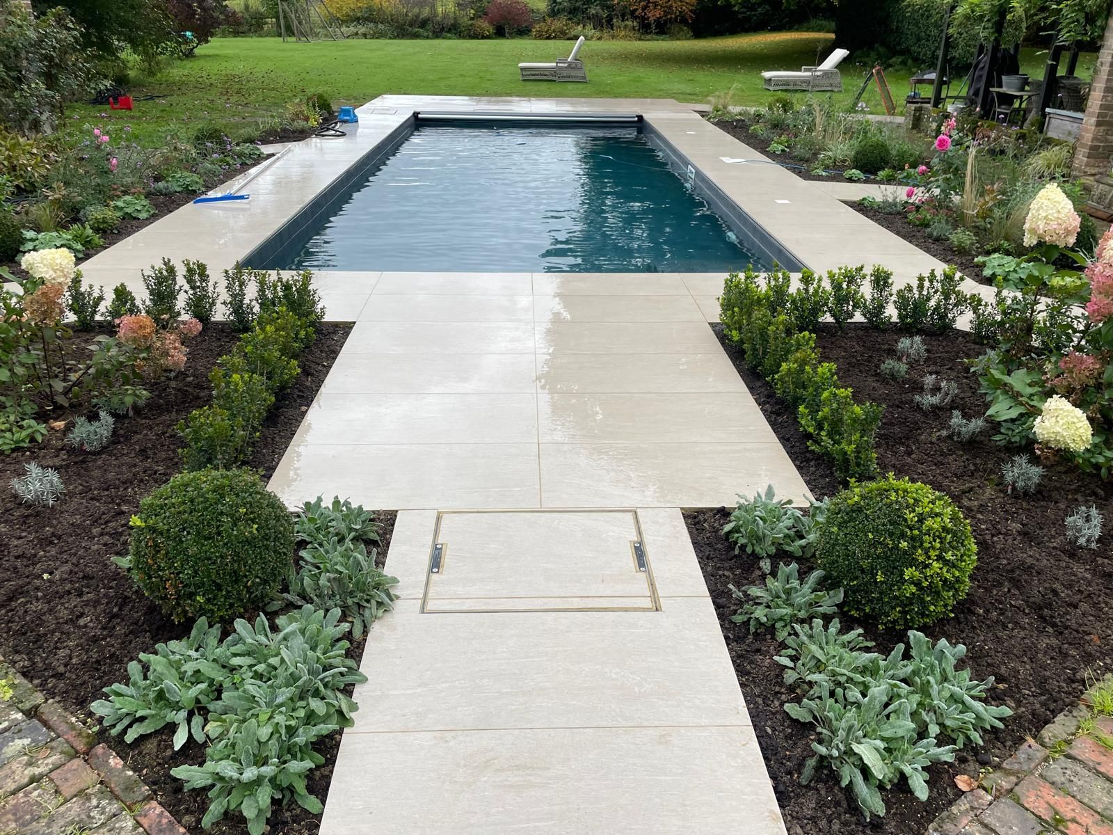 There is a large swimming pool in the middle of a garden.