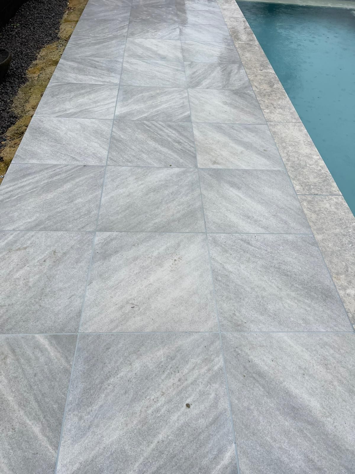 A gray tile walkway next to a swimming pool.
