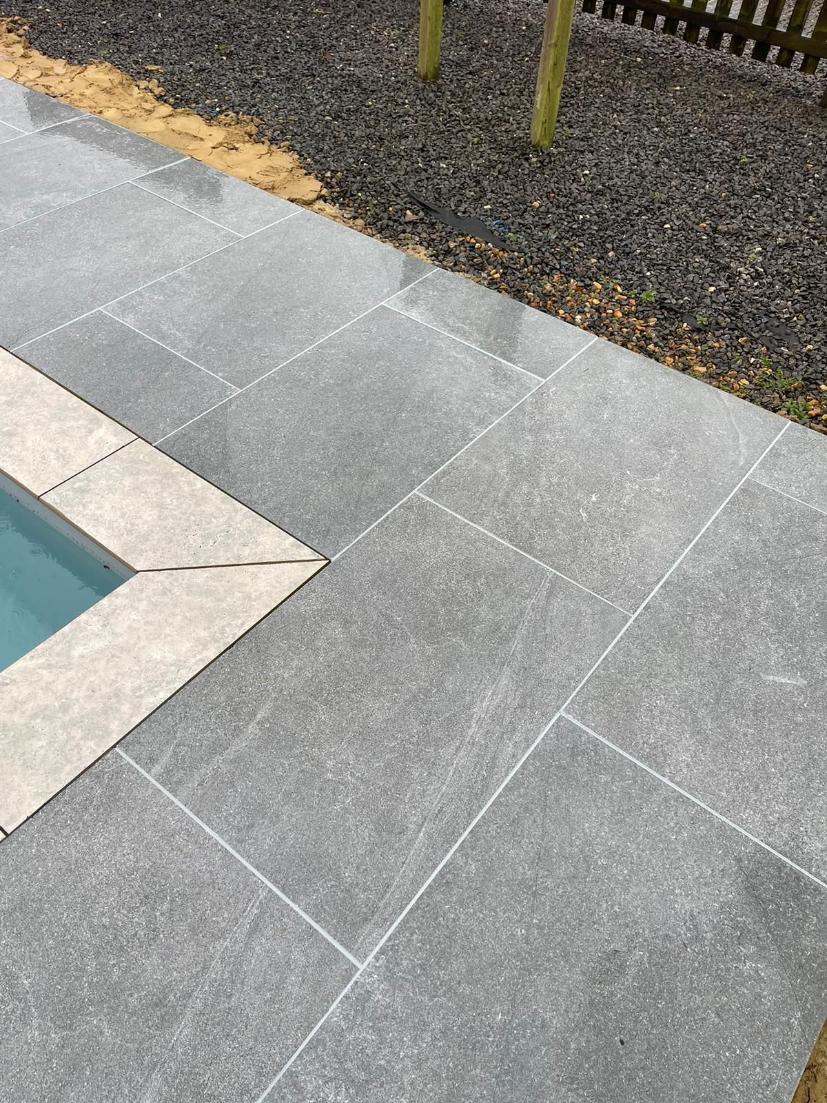 A swimming pool with a tiled patio and a fence in the background.