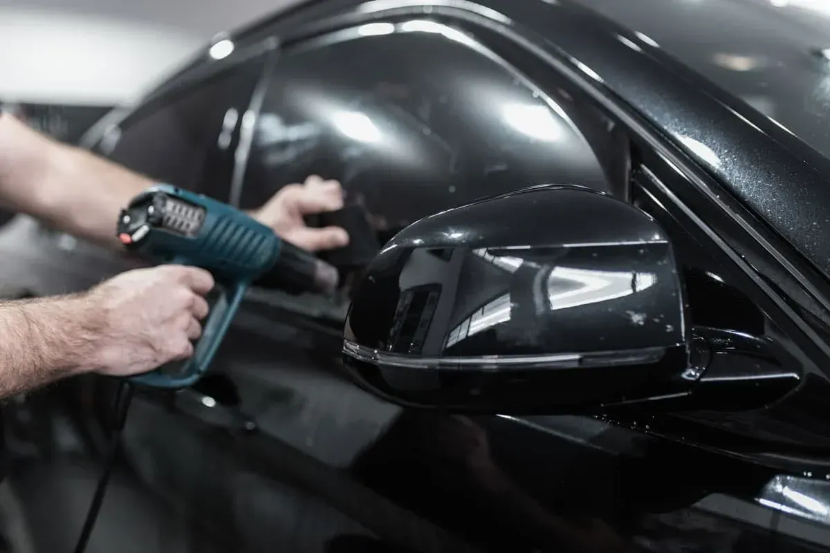 A man is wrapping a red car with a protective film.