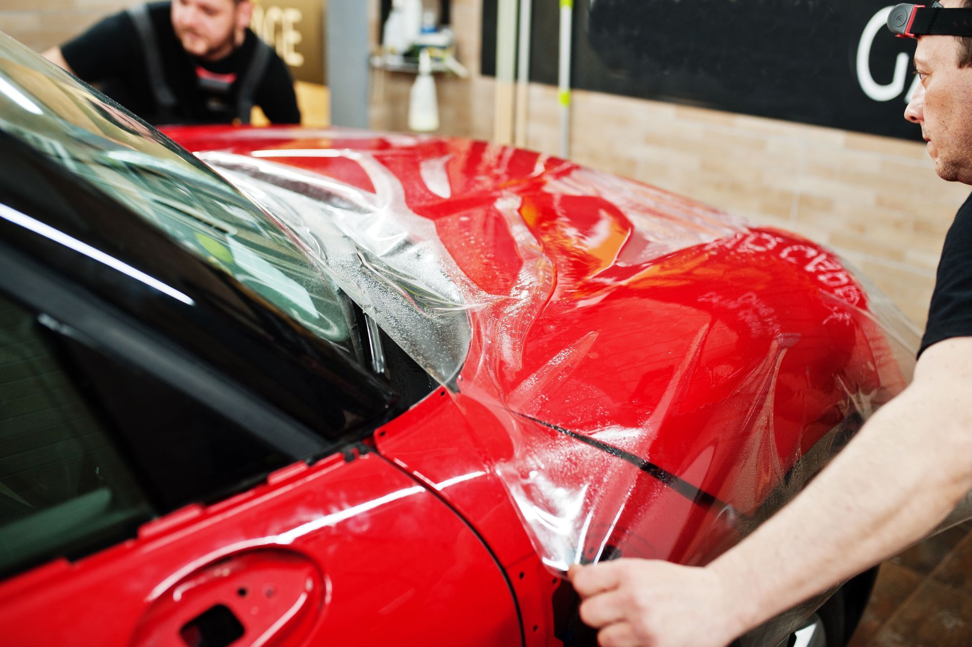 A man is wrapping a red car with a protective film.