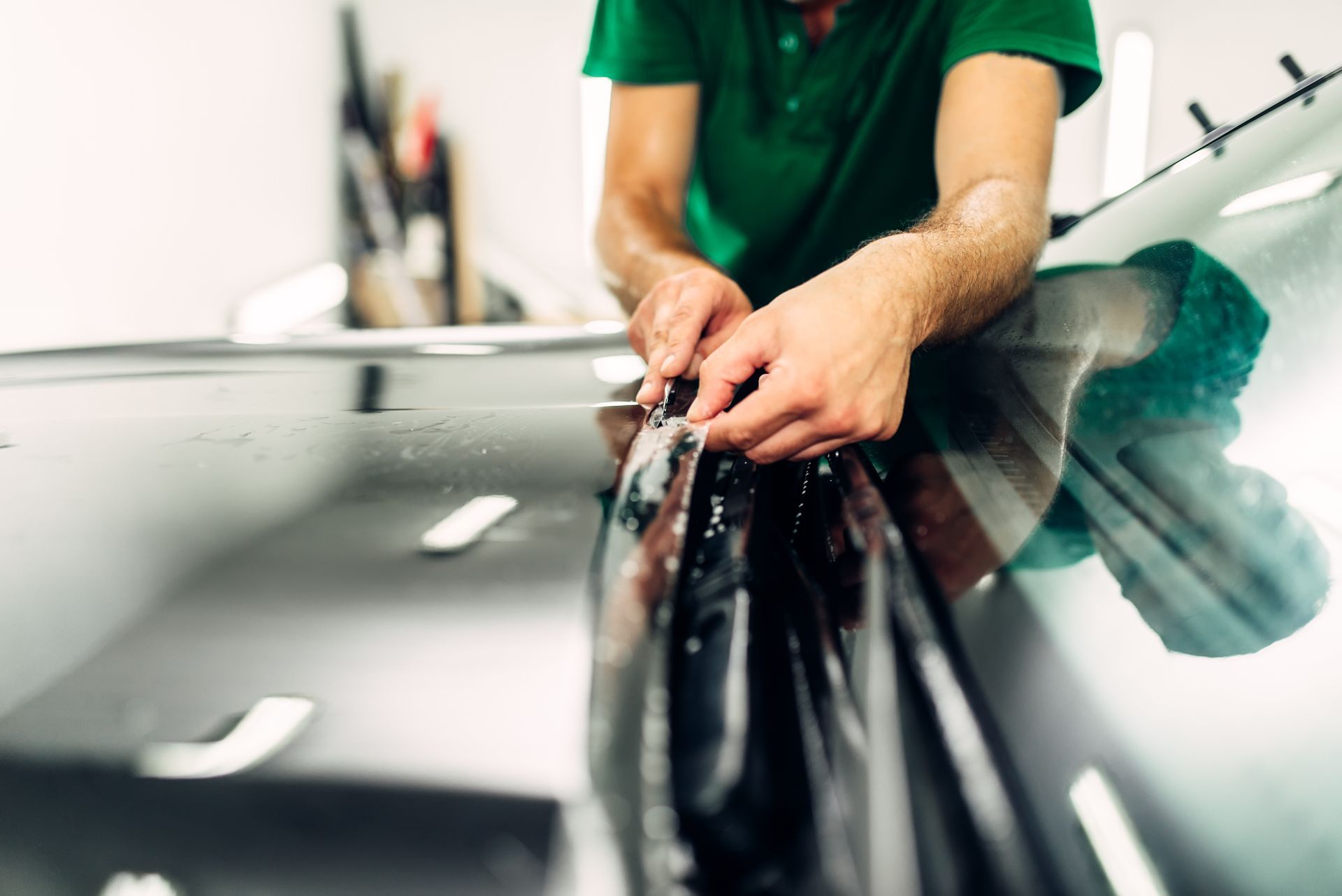 A man in a green shirt is wrapping a car with a film.