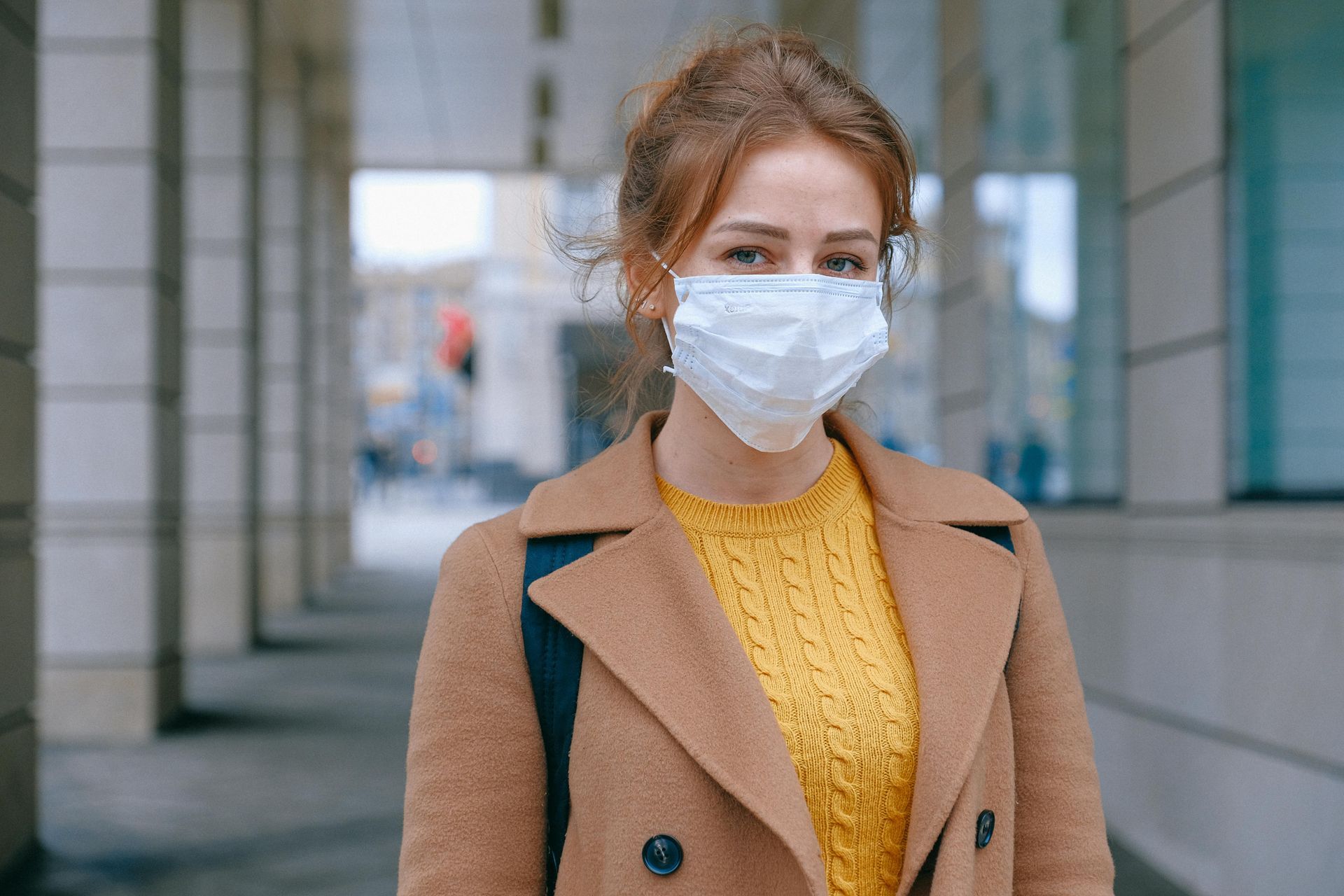 A woman wearing a face mask is standing in front of a building.