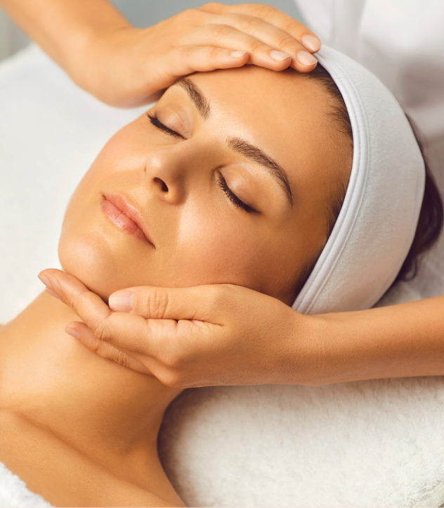 Woman receiving facial massage, eyes closed, hands on face, white headband, spa setting.