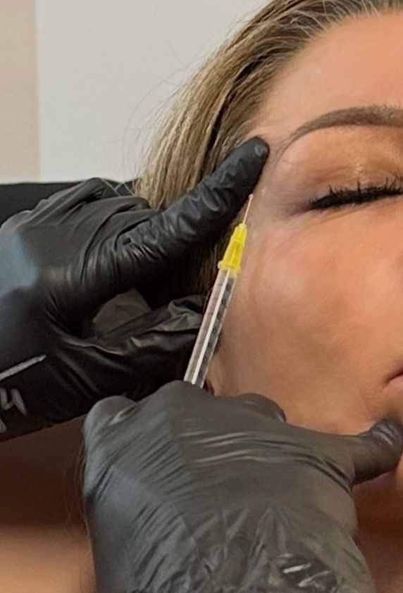 A person receiving a facial injection from someone wearing black gloves, in a clinic setting.