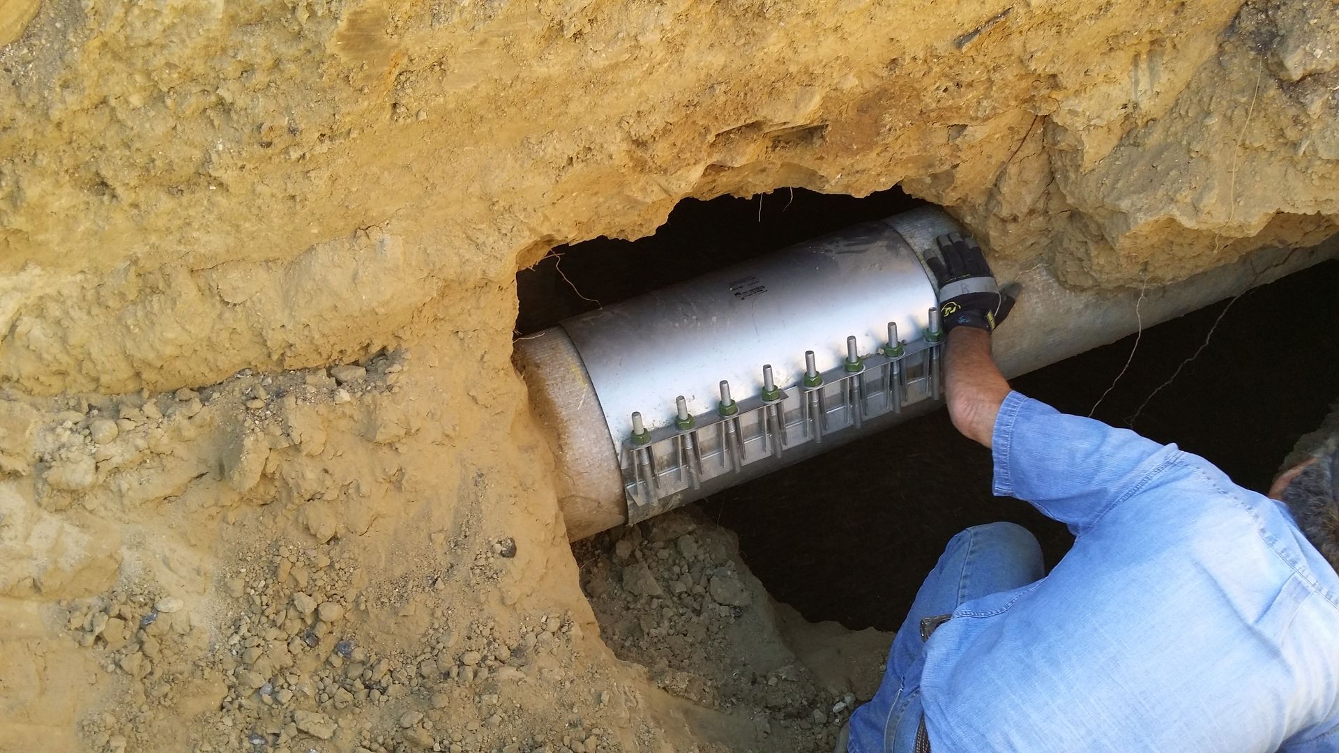 Man inspecting a large white pipe in a dirt trench, likely for maintenance or repair.