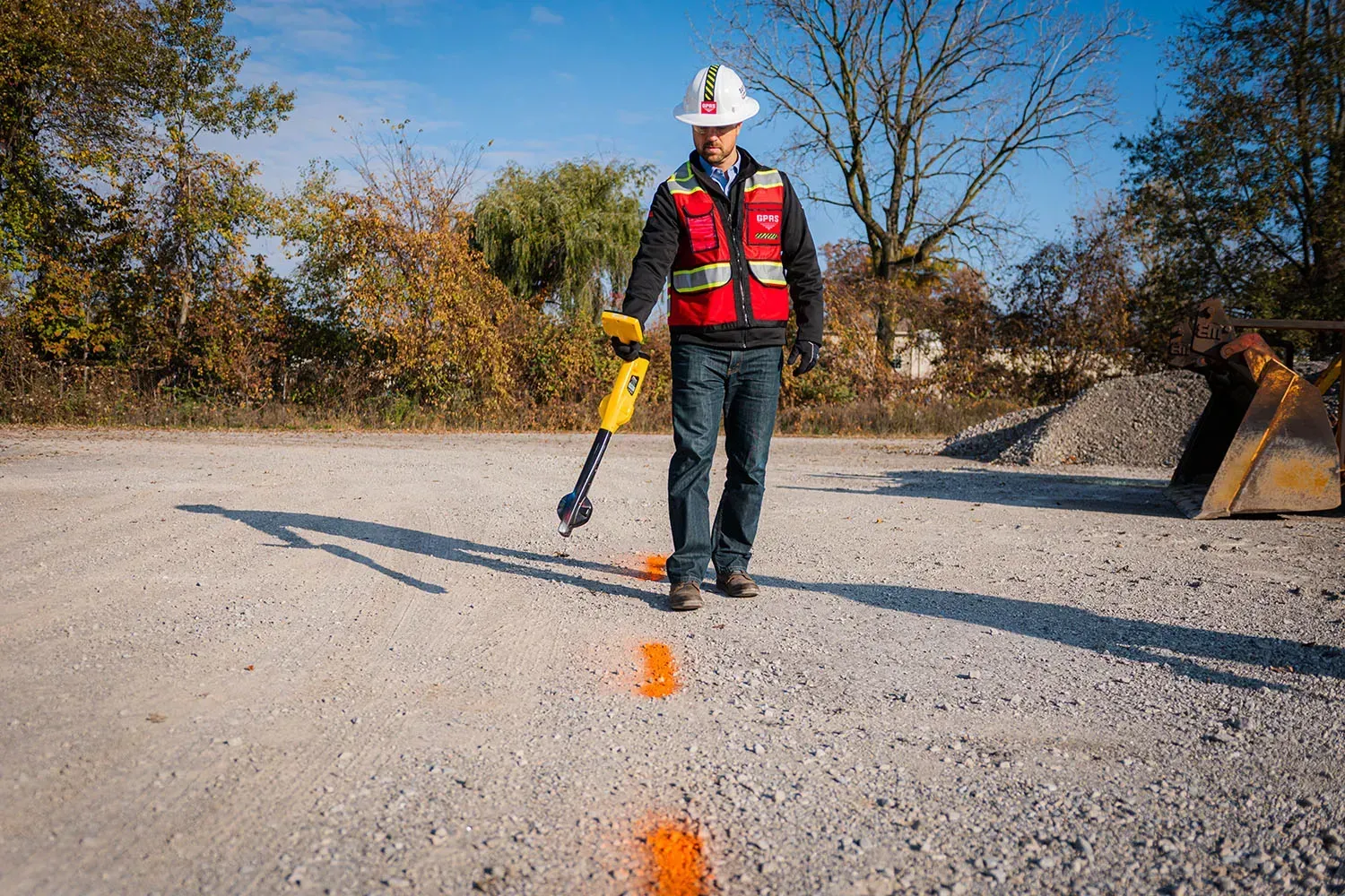 A person using a detection tool outdoors, walking over marked pavement.