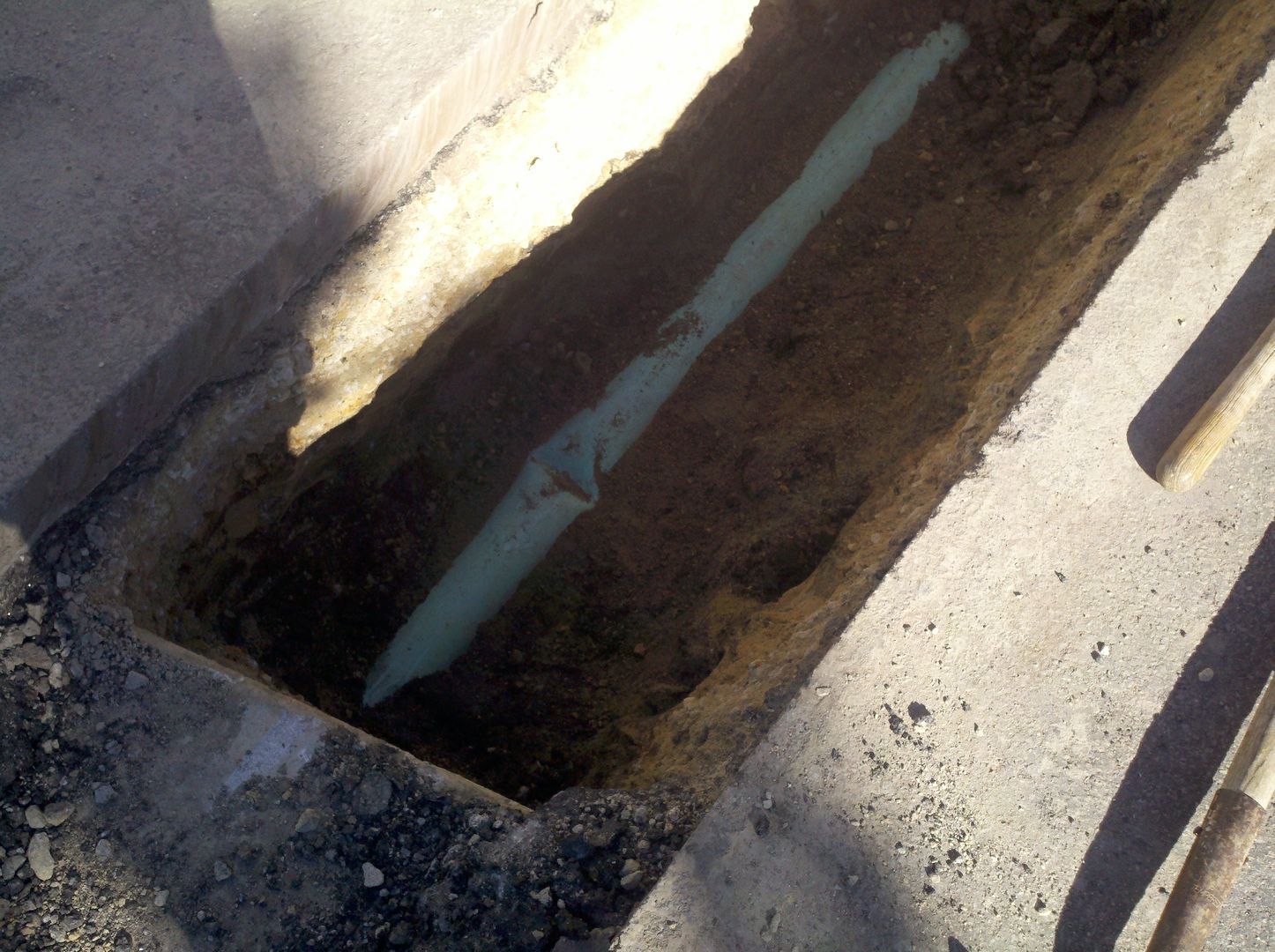 Trench in concrete, containing a light green pipe.