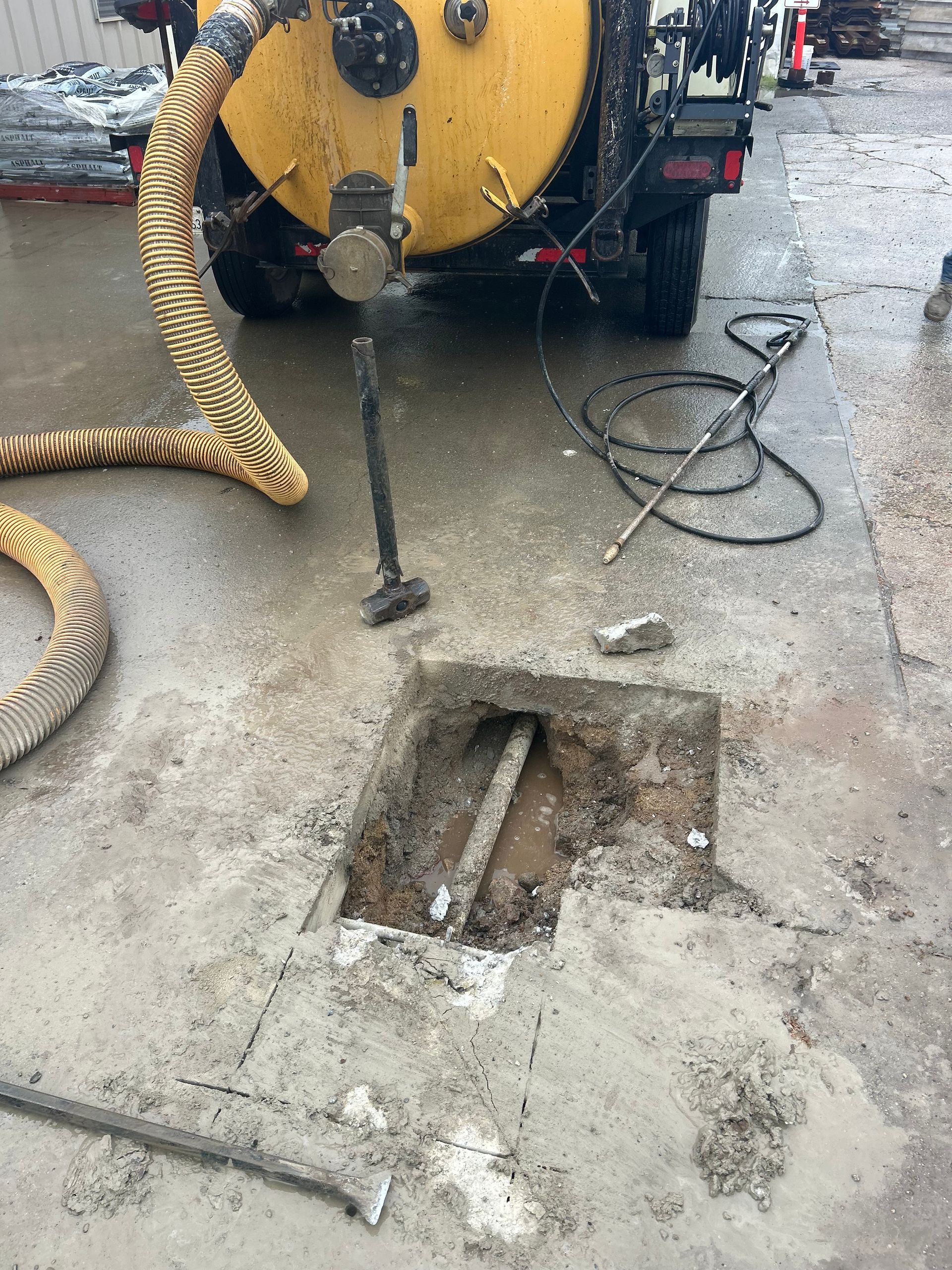 A yellow vacuum truck connected to an open concrete access point on a wet concrete surface.