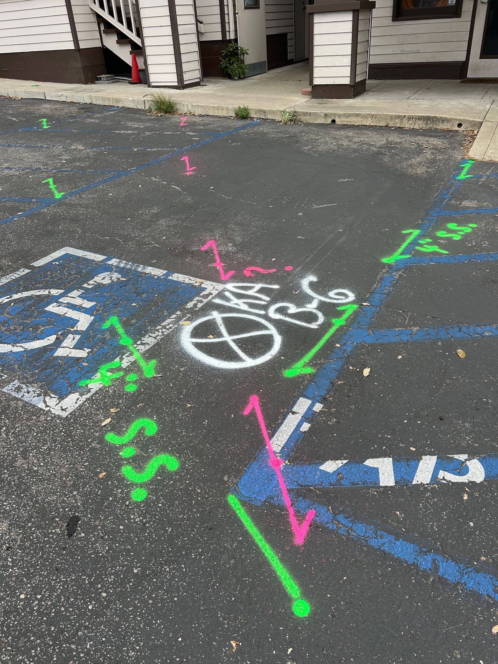Asphalt parking lot with blue handicap space markings and utility markings in pink and green spray paint.