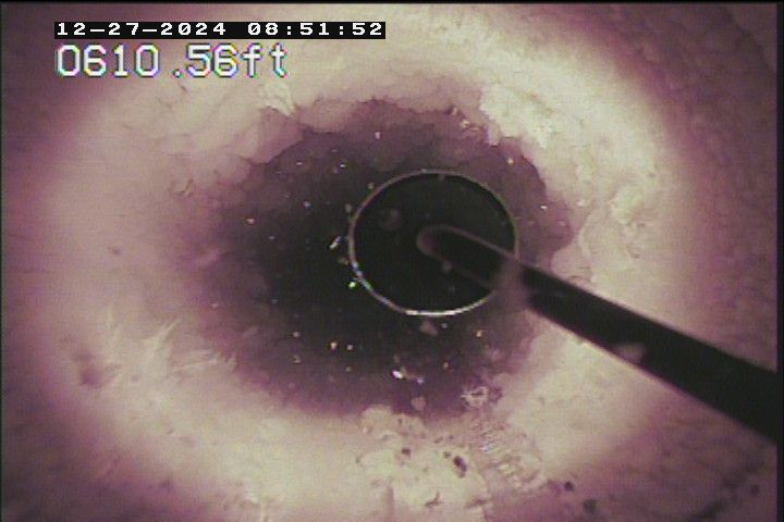 View inside a dark pipe with a tool inserted. White and pinkish inner walls with dark central opening.