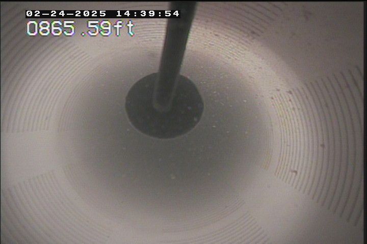 View from within a cylindrical pipe, camera pointed down. A dark probe is centered. Depth reading: 0865.59 ft.