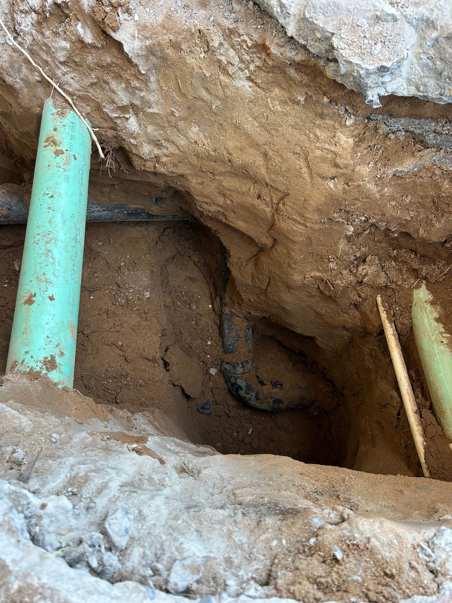 Pipes in a dug trench with earth and rock. Green pipes and dark pipes are visible.