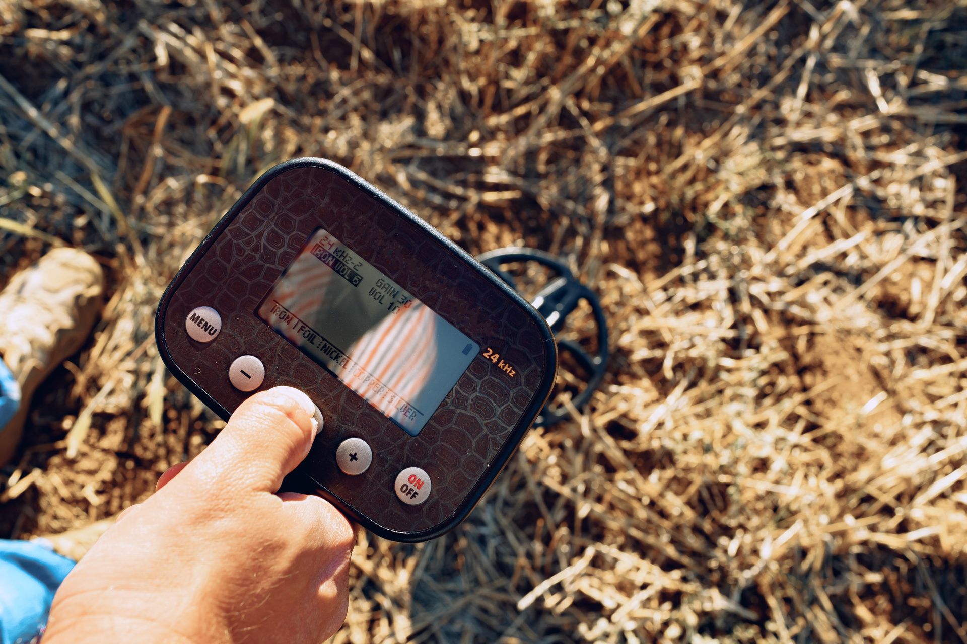 A person using a metal detector in a dry, grassy field.
