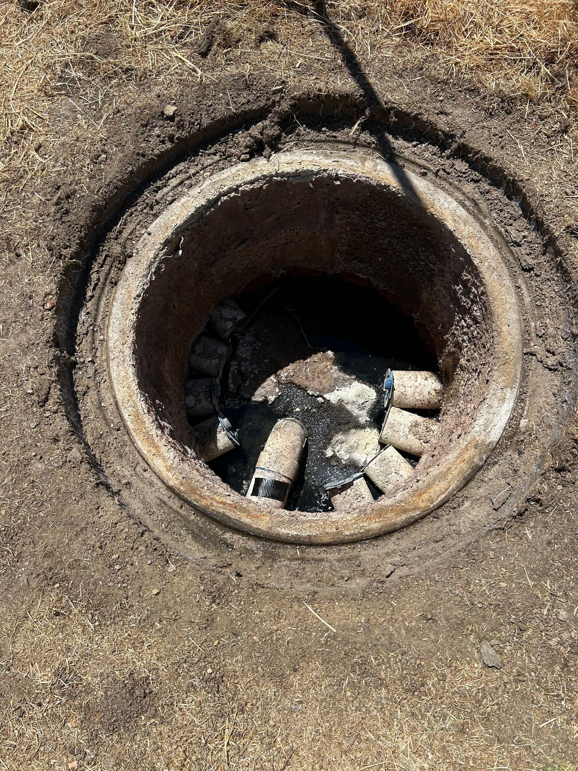 A concrete fire pit with ash and partially burned objects inside, set in the ground.